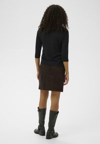 Haut noir à manches longues associé à une jupe en suède marron. Le mannequin porte des bottes en cuir noir montantes avec des talons épais et des accents subtils.