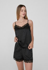 Conjunto de camisón y pantalones cortos de satén negro con lunares blancos, que presenta un borde de encaje en el escote y el dobladillo. Tirantes finos ajustables.