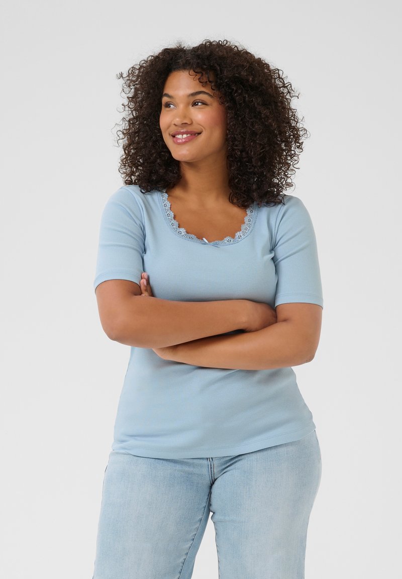 Light blue ribbed t-shirt featuring a scalloped neckline and short sleeves, paired with light denim jeans. Smooth texture and fitted design.