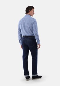 Hellblau kariertes Hemd mit langen Ärmeln, kombiniert mit dunkelblauen Jeans. Die Jeans haben aufgerollte Säume und Gesäßtaschen.