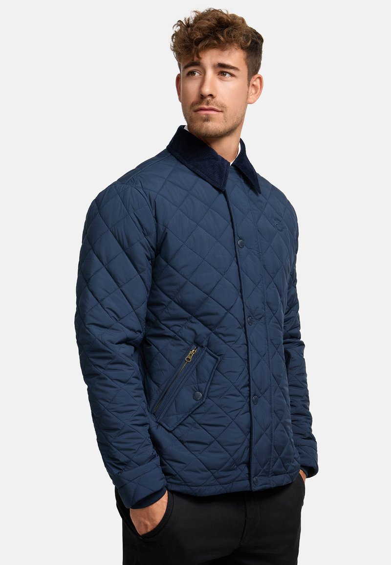 Navy quilted jacket with a corduroy collar, featuring a zippered pocket and button closure, crafted from a smooth, padded synthetic material.
