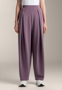 Lila weite Hosen mit Falten, aus glattem Material und mit hohem Taillenbund, kombiniert mit weißen Sneakers.