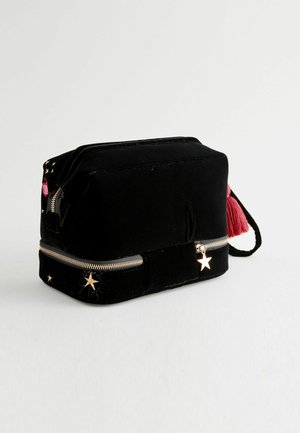 Schwarze Samt-Schminktasche mit goldfarbenem Reißverschluss, bestickten Sternen und einem roten Quastendetail. Rechteckige Form, weiche Textur.
