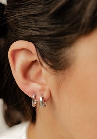Des boucles d'oreilles anneaux en argent pendent d'une oreille humaine, présentant une finition lisse et polie avec un design légèrement torsadé et une texture brillante.