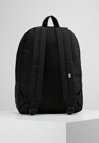 Sac à dos noir avec bretelles rembourrées et poignée de transport, présenté de dos sur une surface blanche avec un fond gris clair.