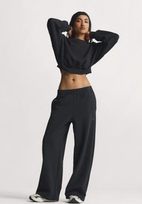 Crna skraćena majica s širokim rukavima, uparena s crnim širokim joggericama s elastičnim pojasom i bočnim džepovima.