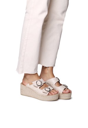Wedge sandals with a beige textured upper, two adjustable buckles, and a woven jute heel. Paired with cropped white pants.