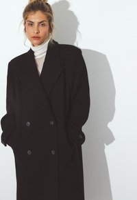 Čierny dvojradový kabát z hrubej tkaniny. Má výrazné klopy, dva gombíky a veľké vrecká. Nosený cez svetlý rolák.