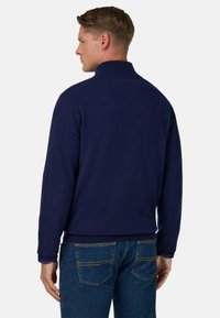 Marineblaue Jerseyjacke mit geripptem Kragen und Bündchen, zeichnet sich durch eine glatte Textur und klare Linien aus, kombiniert mit blauen Jeans.