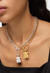 Collares de cadena en capas con un colgante de oso plateado y uno dorado, con eslabones metálicos alternados. Texturas lisas y brillantes.