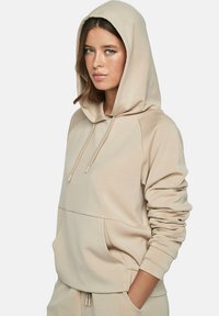 Beige hoodie met een trekkoord capuchon, kangoeroezak en geribbelde manchetten. Zachte stof met een gladde textuur en een relaxed fit.