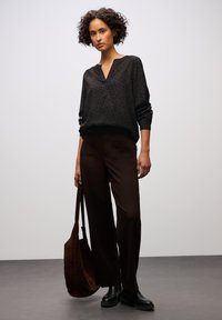 Schwarze Leopardenmuster-Bluse mit V-Ausschnitt, kombiniert mit dunkelbraunen weiten Hosen. Braune Wildleder-Schultertasche und schwarze Ankle Boots.
