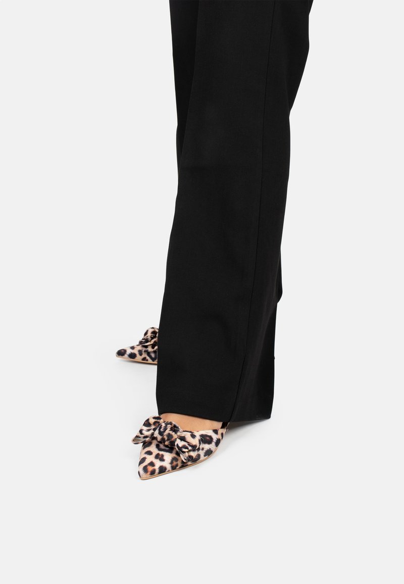 Leopardenmuster High Heels mit spitzer Zehe und einer Schleifendetail an der Vorderseite, kombiniert mit weiten schwarzen Hosen. Glatte Stofftextur.