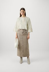 Light-colored, textured top with frayed accents, paired with a long, beige denim skirt. Accessorized with a white handbag and gray boots.