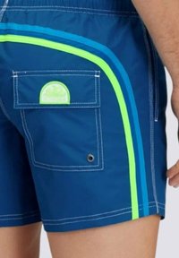 Pantaloni da bagno blu navy con righe laterali verdi e blu. Presentano una tasca sul retro con un logo circolare e dettagli con occhioletto in metallo.