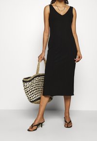 Czarna, prążkowana sukienka midi z dekoltem w serek i wąskimi ramiączkami. Towarzyszy jej pleciona torba ze słomy z czarnym wykończeniem oraz klapki.