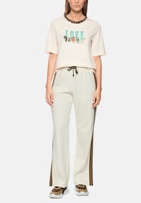 Cream short-sleeve T-shirt with a leopard print collar and “LOVE” graphic. Paired with pale beige tracksuit pants featuring side stripes.