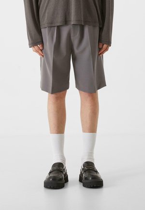 Grå shorts med folder, kombinert med hvite sokker og svarte sko. Toppen har et langermet, stripet design i dempede farger.
