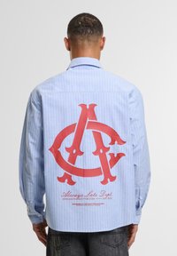 Blue and white striped button-up shirt with a large red graphic logo on the back. Features long sleeves and button closures on cuffs.