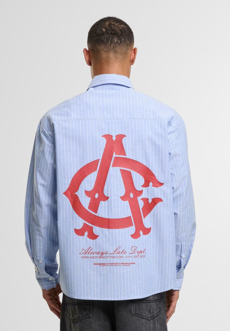 Blue and white striped button-up shirt with a large red graphic logo on the back. Features long sleeves and button closures on cuffs.