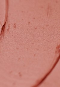 Produit cosmétique crémeux de couleur pêche, à la texture lisse, présentant des variations subtiles d'ombre et une finition légèrement brillante.