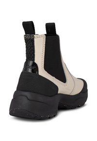 Beige och svart ankelsko med elastiska sidopaneler, texturerade detaljer och gummisula. Har vävt detaljer nära hälen.