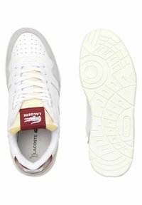 Sneaker bianche con accenti grigi, texture perforata sulla punta, lacci bianchi e un'etichetta rossa con il marchio sulla linguetta. La suola presenta pattern di trazione.