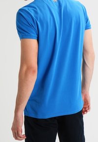 Kurzarm-T-Shirt aus leuchtend blauem Baumwollstoff, mit Rundhalsausschnitt und schlichtem Design, das minimale Nahtdetails an den Ärmeln aufweist.