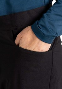 Schwarze Hose mit einer Seitentasche, kombiniert mit einem blauen Langarmshirt. Der Stoff wirkt glatt, mit einem figurbetonten Design an der Taille.