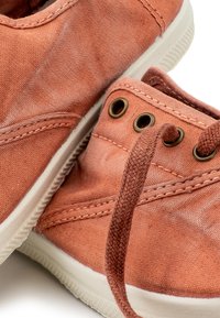 Világos korall színű vászon sportcipők fehér gumi talppal, bronz fűzőlyukakkal és texturált fűzőkkel, enyhe eltérésekkel az anyagban.