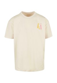 Kremowa bawełniana koszulka z krótkim rękawem, okrągłym dekoltem i małą, kolorową grafiką "hi" na lewej stronie klatki piersiowej.