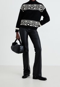 Svart stickad tröja med vita geometriska mönster, ihop med svarta byxor i konstläder med vida ben och en svart handväska. Slät textur, avslappnad passform.