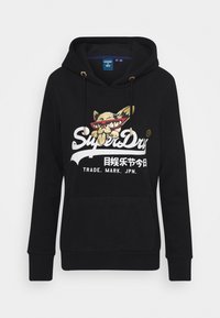 Černá mikina s kapucí a přední kapsou, s grafikou zlaté a červené barvy znázorňující kočku v brýlích a textem "SuperDry" v bílé barvě.