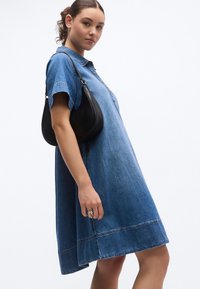 Galléros, rövid ujjú, kényelmes szabású farmerruha. Világoskék színű, látható varrási részletekkel. Fekete válltáskával kiegészítve.