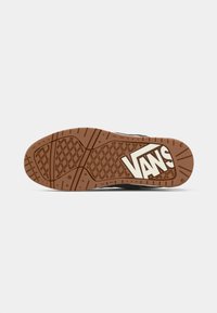 Baskets noires avec une semelle extérieure en caoutchouc marron présentant un motif de semelle en gaufre et le logo "VANS" en blanc. Le matériau semble texturé et durable.