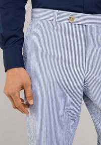 Striped trousers with a light blue and white pattern, featuring a button closure, belt loops, and a side pocket. Cotton fabric texture.