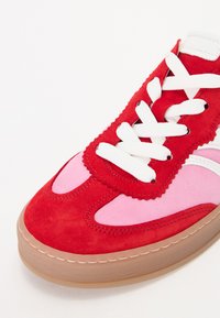 Sneaker in suede rosso e rosa con lacci bianchi, accenti testurizzati e suola in gomma. Presenta dettagli a ondulazione lungo i bordi superiori.
