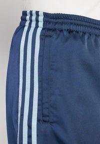 Pantalones cortos deportivos de color marino con rayas verticales en azul claro, cinturilla elástica y un bolsillo lateral para almacenamiento. Tejido suave y ligero.