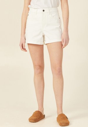 Shorts en denim blanc avec revers, taille haute et fermeture à boutons à l'avant. Assortis à des chaussures à enfiler en daim marron.