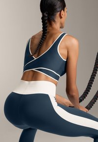 Mornarsko modra športna srajca z belimi poudarki, v kombinaciji z visokimi mornarsko modrimi legicami, ki imajo bele stranske črte. Gladka tekstura, prilegajoča zasnova.