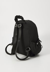 Black fabric backpack with a gathered top handle, adjustable straps, side pockets, and silver hardware. Smooth texture with a minimalist design.