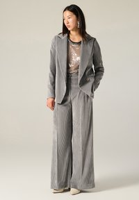 Blazer grigio in corduroy e pantaloni a gamba larga abbinati a un top con paillettes. I dettagli degni di nota includono un colletto, chiusura con bottoni e orecchini a forma triangolare.