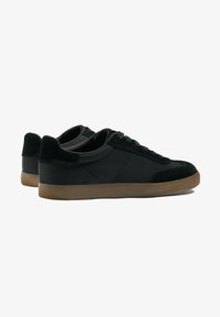 Black sneakers with a smooth leather and suede upper, round toe, and textured gum rubber sole. Features black laces and contrast stitching.