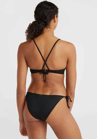 Set bikini nero con bralette triangolare caratterizzato da spalline incrociate e chiusura a fiocco sul retro, abbinato a culotte a vita bassa con lacci laterali.