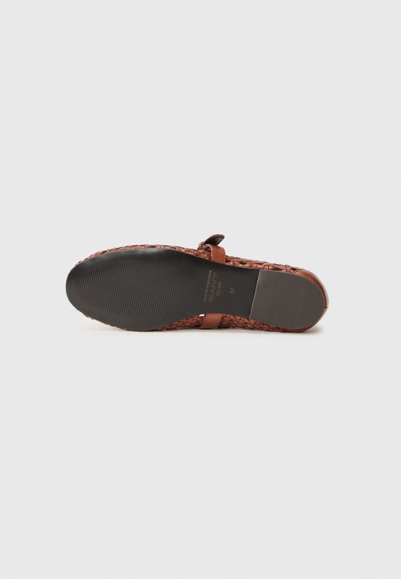 Mocassin en toile brun avec une semelle en caoutchouc plate et une sangle minimaliste sur le cou-de-pied. Tige texturée et intérieur lisse.