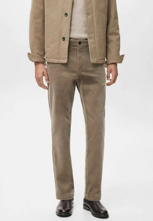 Pantalones de pana beige de corte recto, con cierre de botón y bolsillos delanteros, combinados con un suéter claro y botas de tobillo oscuras.