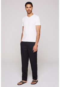 Camiseta blanca de algodón con cuello en V combinada con pantalones de lino oscuros, sandalias planas, presentando un ajuste relajado y un diseño simple sin patrones ni adornos.