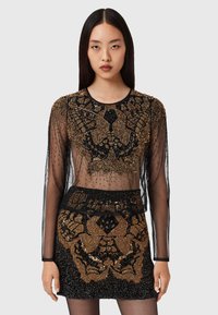 Schwarzes, durchsichtiges Oberteil und Minirock, verziert mit goldenen und schwarzen komplizierten Perlenarbeiten und Mustern. Lange Ärmel, runder Halsauschnitt, körperbetontes Design.
