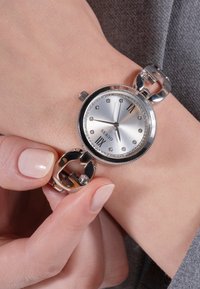 Silver Guess wristwatch with crystal hour markers on wrist, held by hand adjusting the bracelet clasp.