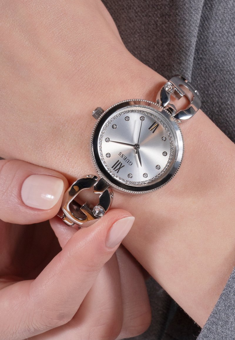 Silver Guess wristwatch with crystal hour markers on wrist, held by hand adjusting the bracelet clasp.